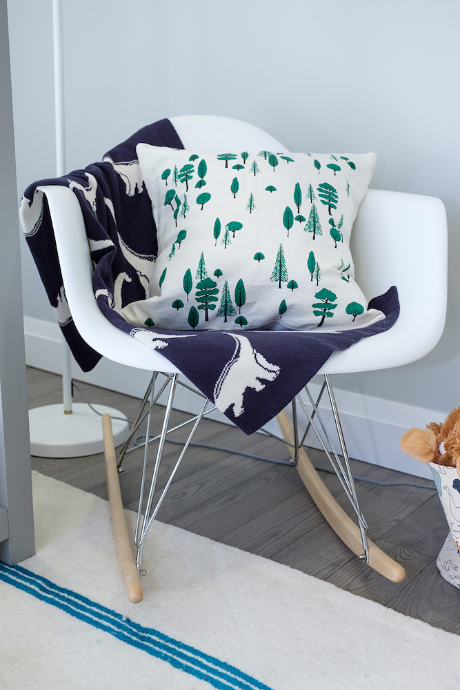 White shell rocking chair with a white tree pillow and blue dinosaur throw