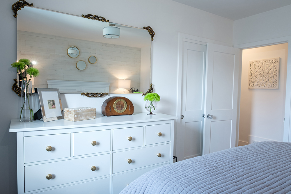 Modern master bedroom with large white dresser and an antique mirror