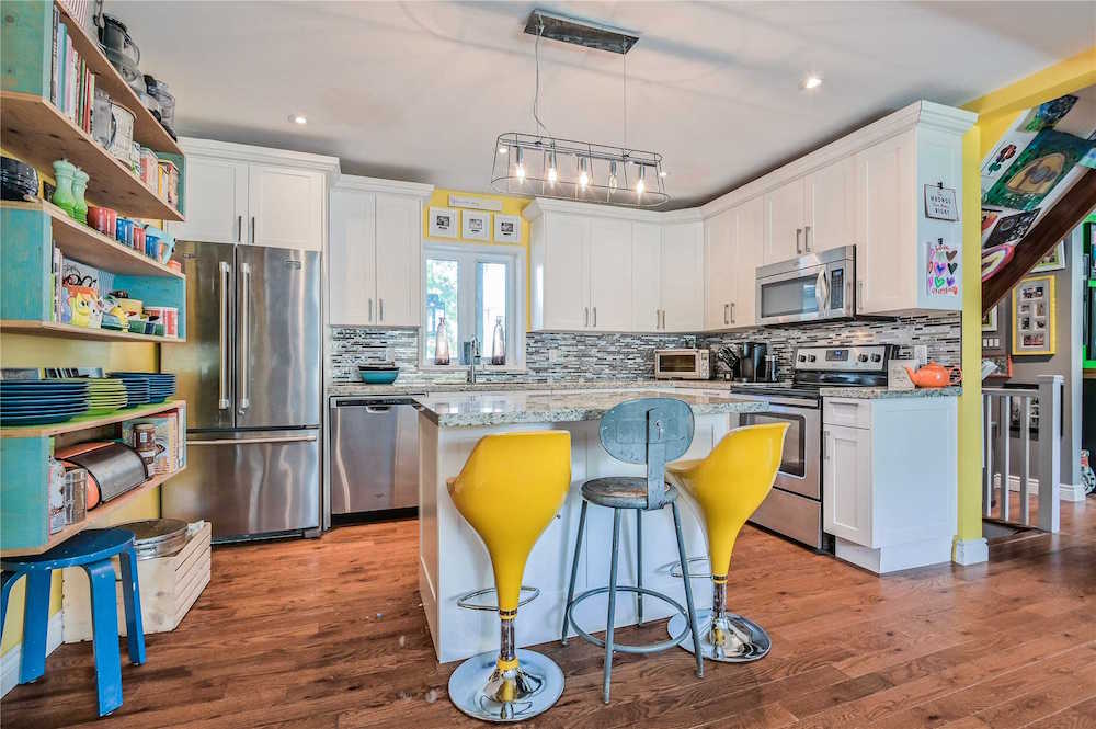 white kitchen with stainless steel appliances and bright yellow bar stools at a centre island