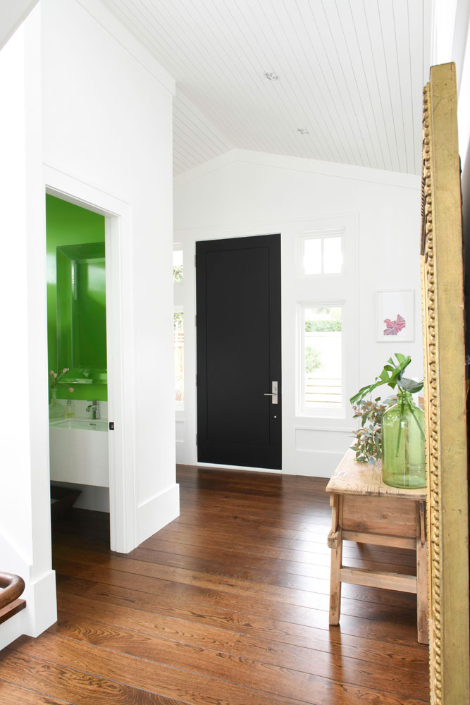front white hall with black door and green accents into powder room