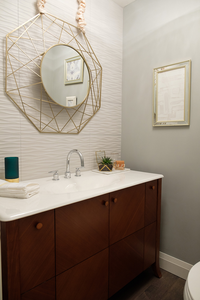 Modern bathroom with a teak vanity, white countertop and a gold mirror