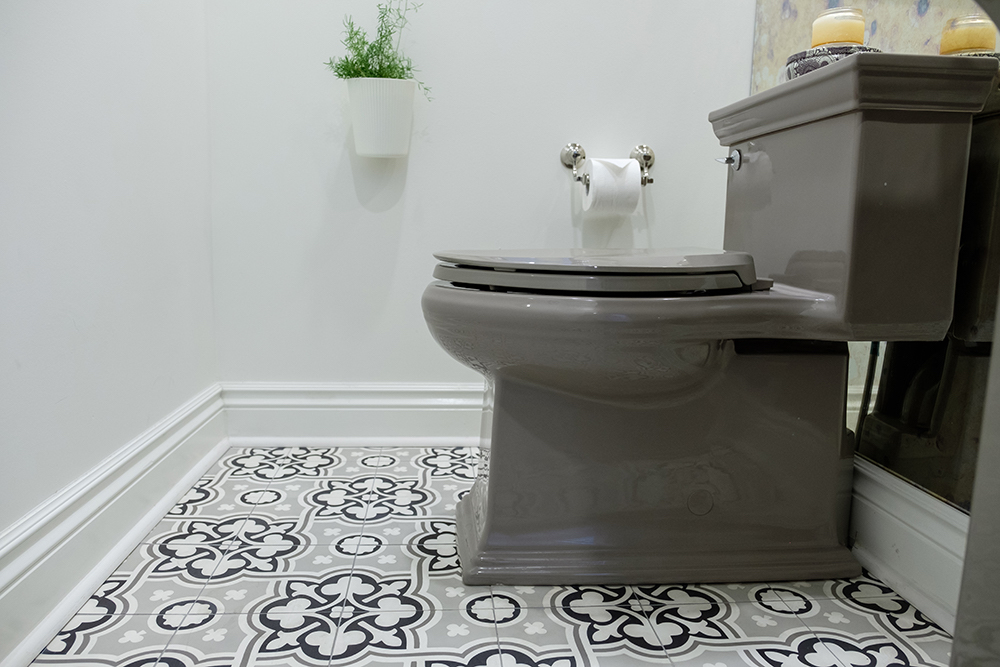 A grey toilet sits on top of a grey-white-and-black patterned bathroom floor tile