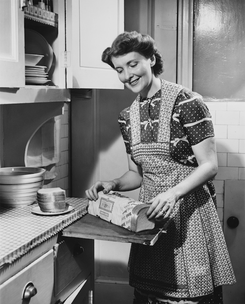 Woman cutting bread in 1950s kitchen