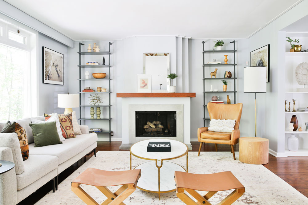 Living room with fireplace flanked by metal shelves, tan chair and two tan stools