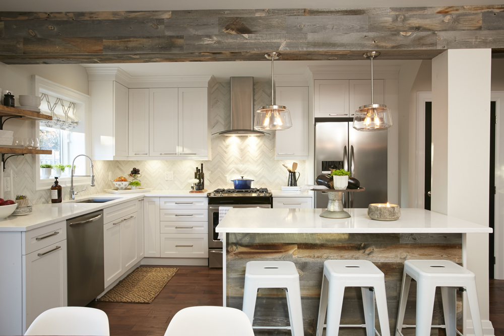 Beautiful white kitchen with white cabinets, countertop and bar stools sitting at a white island with reclaimed barn wood paneling and a large wood clad beam with two statement pendant lights