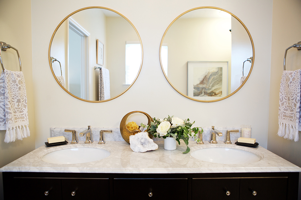 Chic bathroom with double sink vanity, two round gold mirrors and gold faucets and taps
