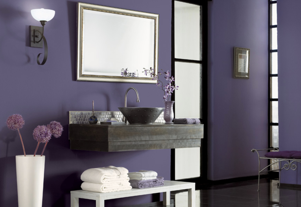 Beautiful bathroom with a floating vanity, a round sink, a silver framed mirror, a white bench stacked with towels, and walls paint in BEHR Hyacinth Arbor PPU16-18 and Carbon N520-7