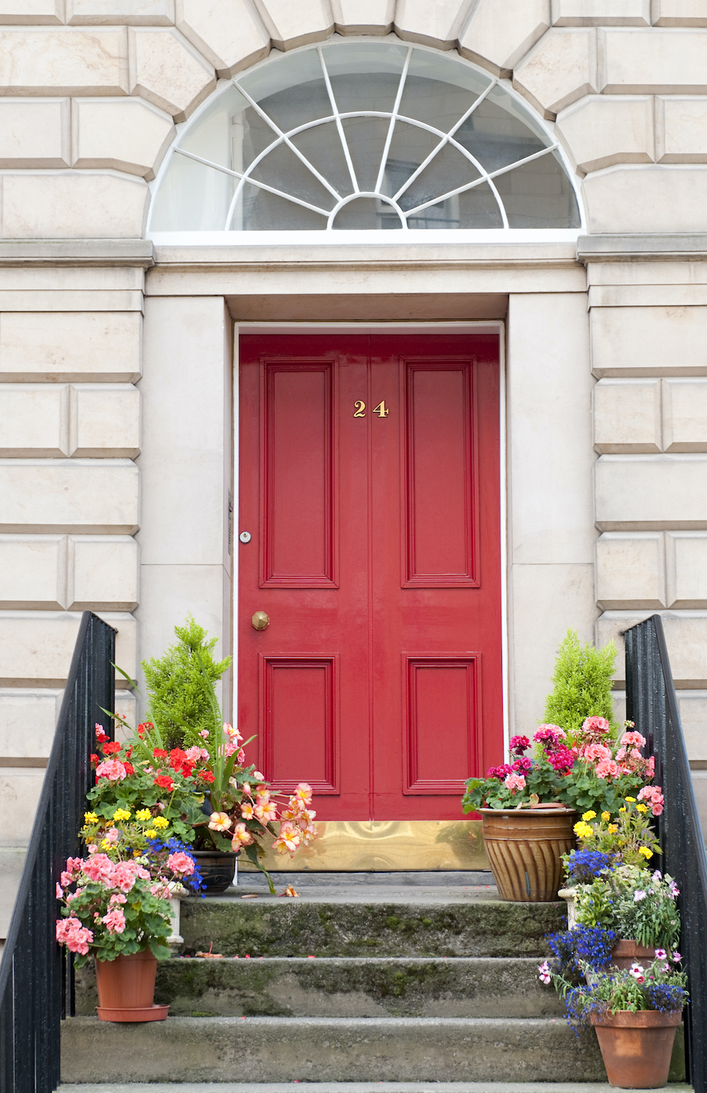 Flowers decorating the steps in front of a red door with brass 21 numerals on it in a grand white house
