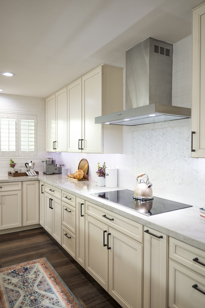 New white kitchen with traditional off white shaker cabinets with black handles, white subway tile backsplash and stainless steel oven hood