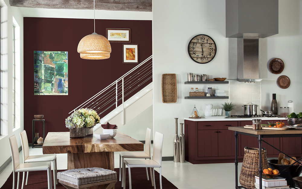 Chic open plan kitchen and dining room with white wood floors, large wood dining table with four white chairs, and cabinets and an accent wall painted burgundy with BERH Dressed To Impress MQ1-19