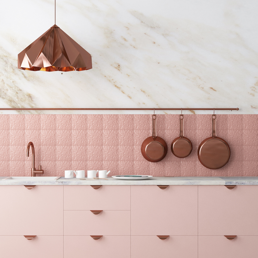Sweet modern loft kitchen with dusty pink cabinets and backsplash, marble wall, rose gold hardware and faucet, and copper pans hanging on a wall railing, and a copper light fixture hanging from the ceiling