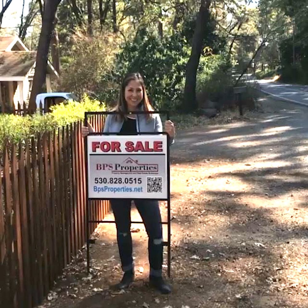 Rustic Rehab host Chenoa Rivera stands behind a for sale sign
