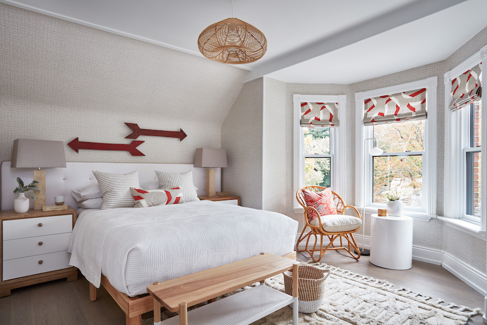 Contemporary bedroom with large wooden bed, two red arrow wall hangings, a wood bench and three bay windows