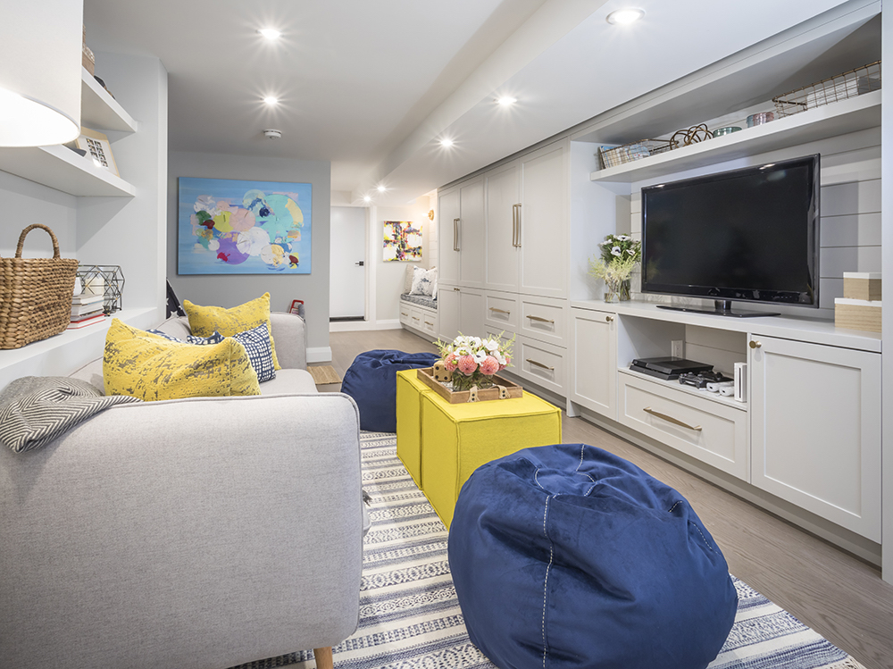 Modern basement family room with large TV, yellow footstools and two blue bean bag chairs