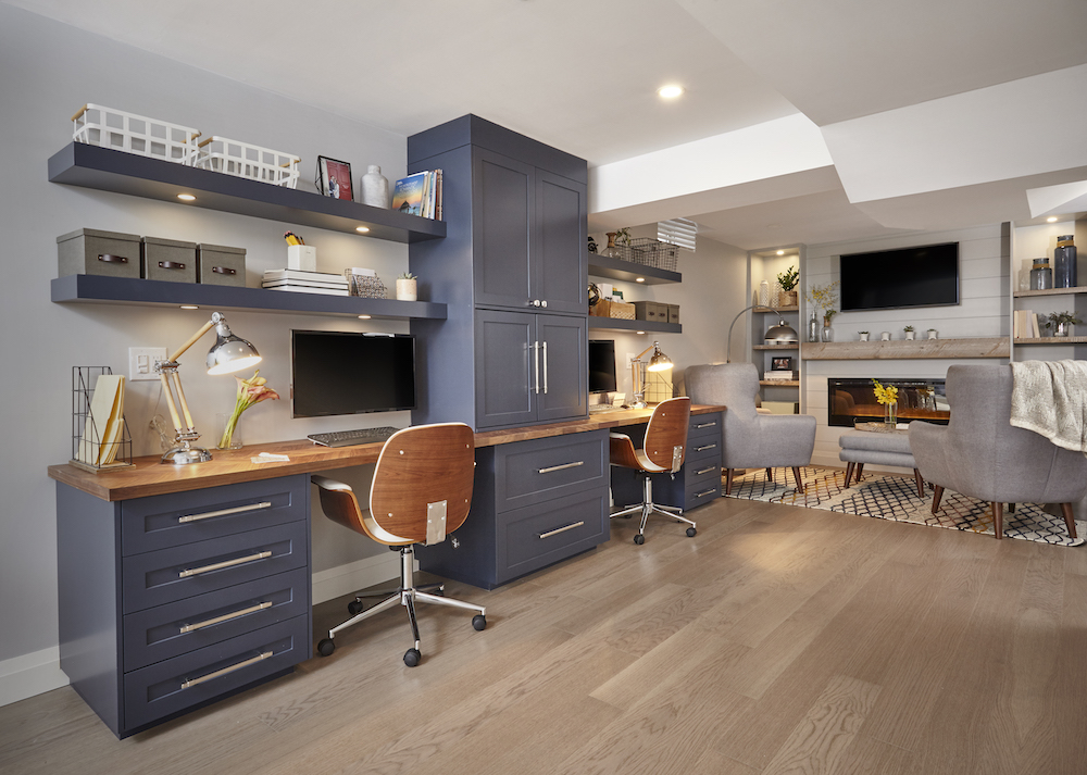 Modern basement home office with a wall of navy blue cabinets, wood tabletop and two wood veneer desk chairs