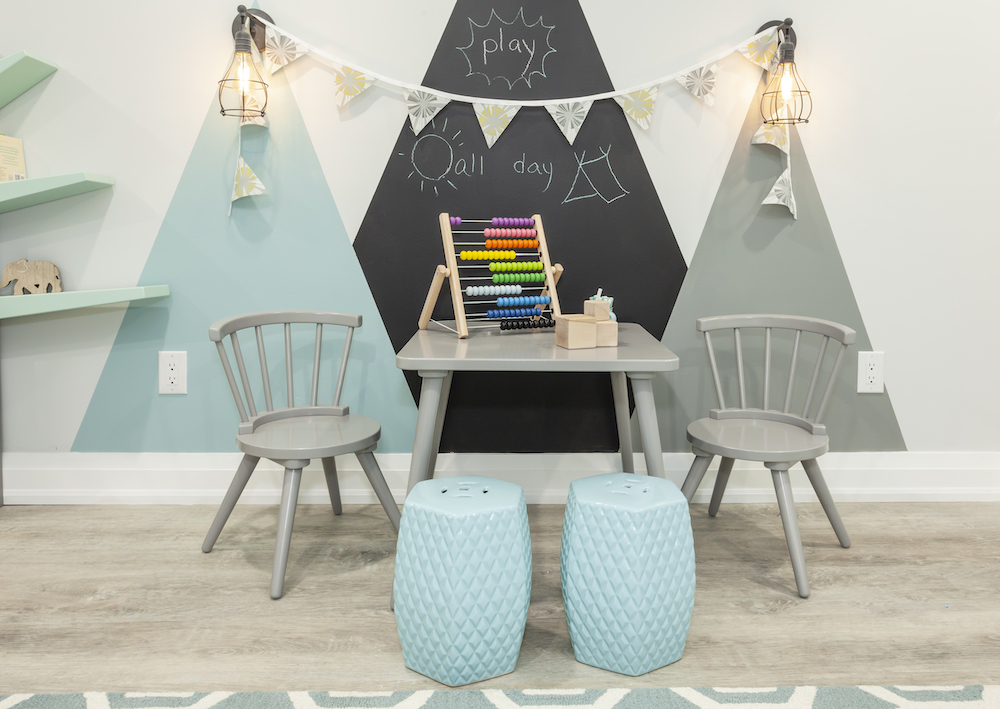 Chic basement playroom with a mountain mural on the wall, a grey play table, two chairs and two blue stools