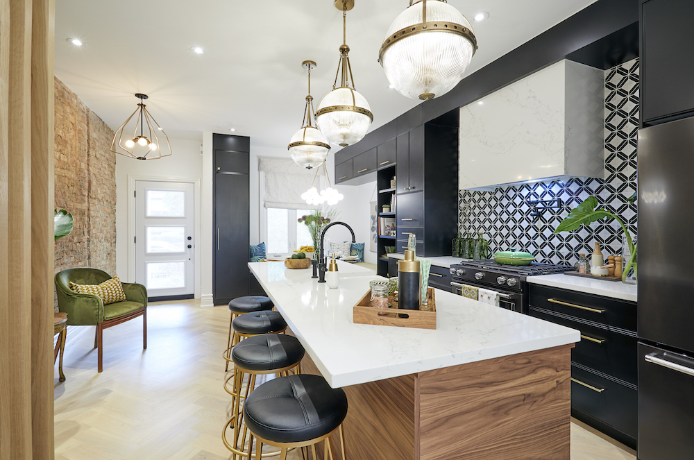 A chic kitchen with black cabinets, a large centre island with a quartz countertop, four bar stools and a black and white tiled backsplash