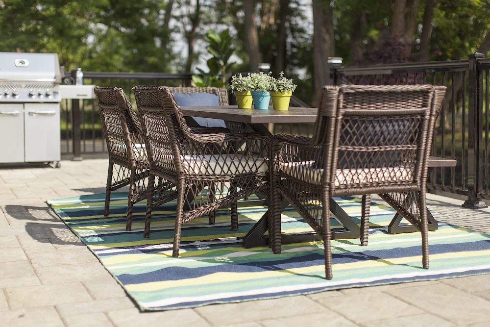 Patio with a brown dining set, blue and green striped outdoor carpet and barbecue in the background