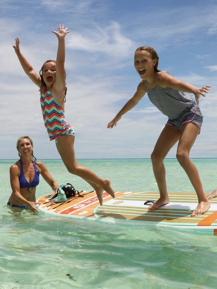 Sarah Baeumler and her two daughters jump off a paddle board in the ocean