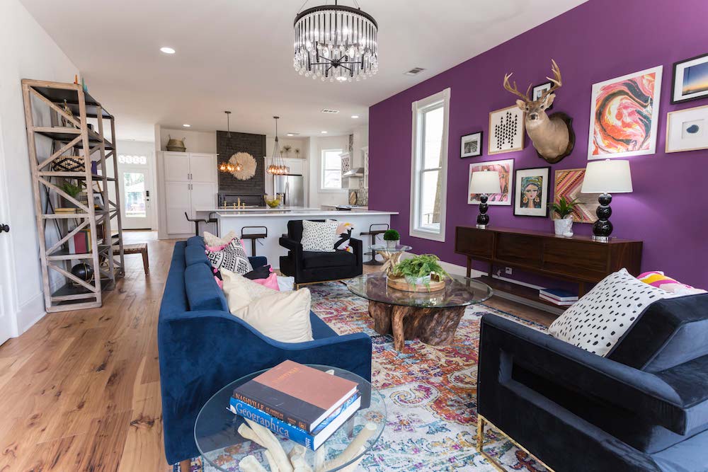 Masters of Flip bohemian Victorian house living room with blue velvet couch and purple wall looking into white kitchen