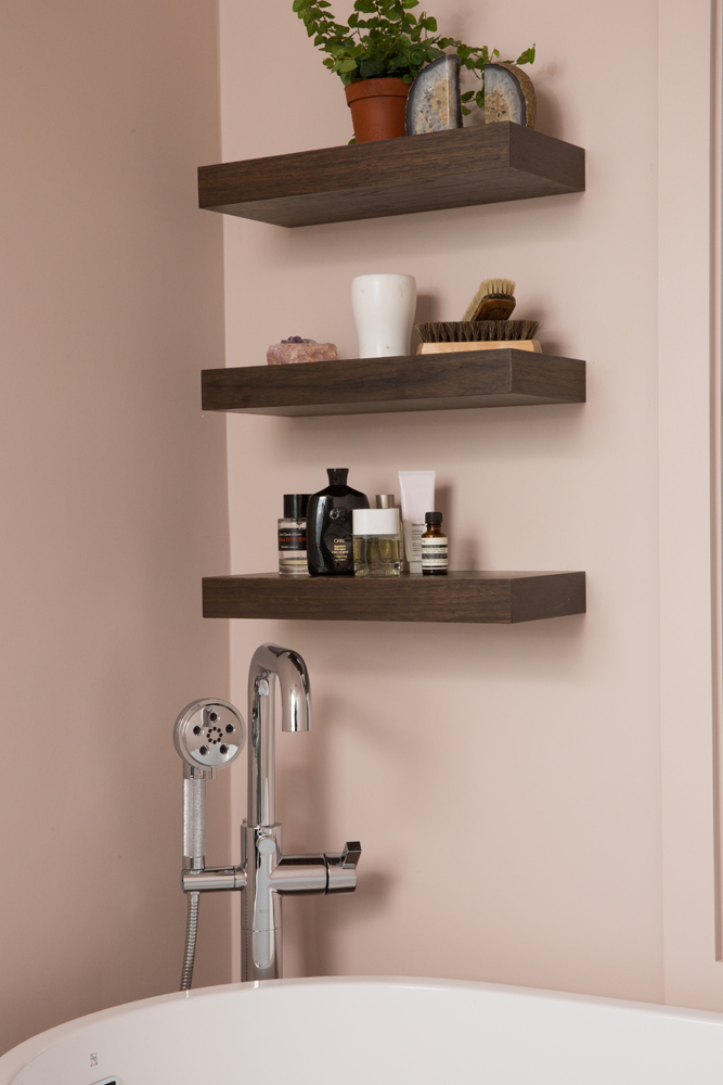 Closeup of three floating shelves above tub in pink bathroom