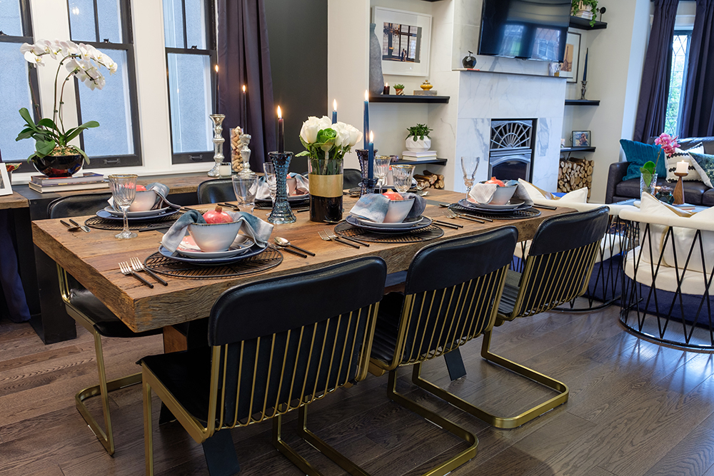 A chic, wooden dining room table set with blue plates and bowls surrounded by black-leather-and-brass chairs