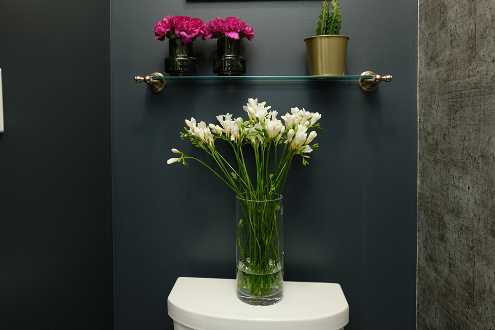 A vase of white flowers sits on a white toilet in a black powder room