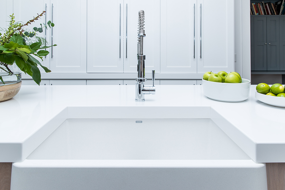 A sleek, white apron sink in a white kitchen.