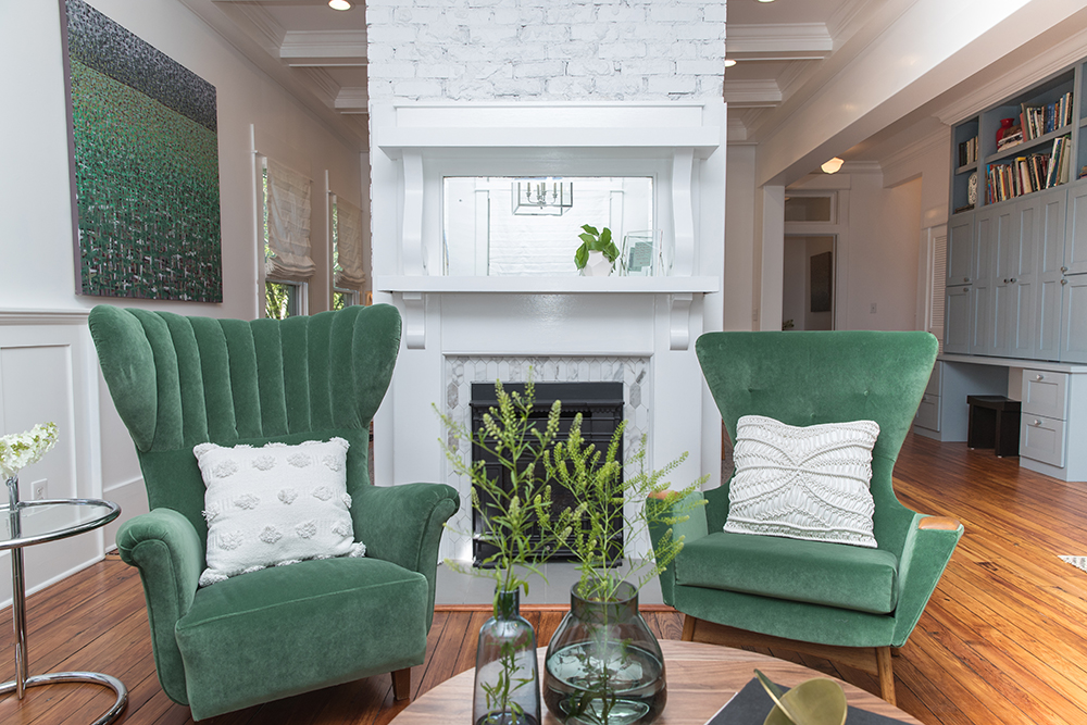 A white, double-sided fireplace with green wing back chairs in a living room.