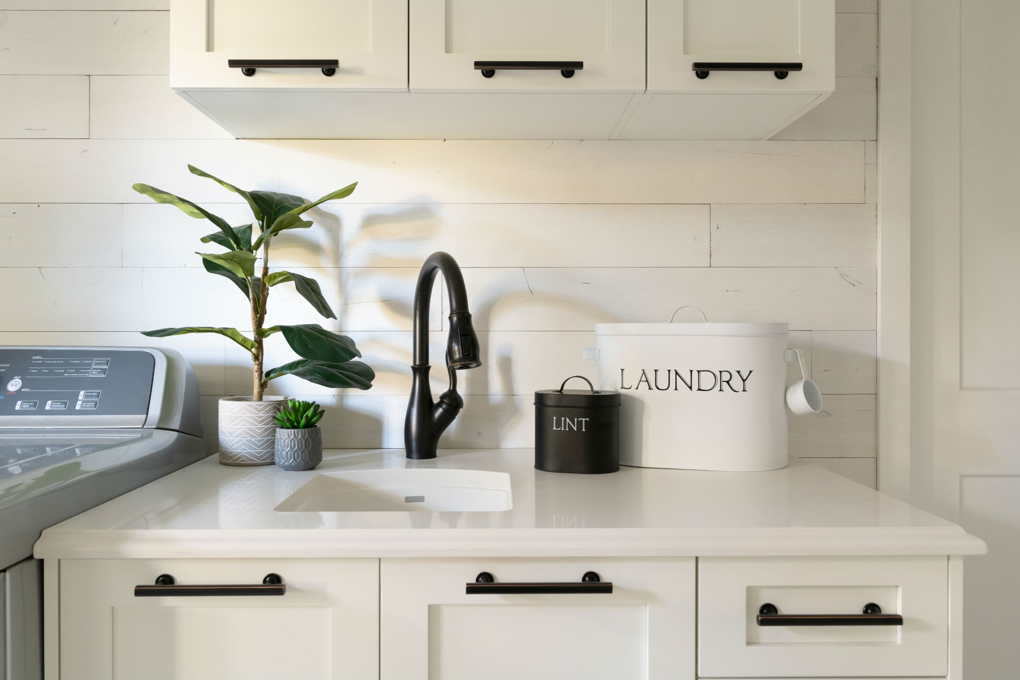 White laundry room with black cabinet hardware and sink fixture