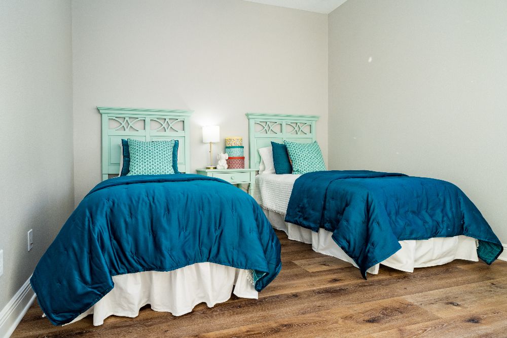 A guest bedroom with twin beds featuring aqua coloured headboards, deep blue duvets, and accent pillows in greens and blues.