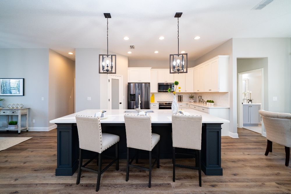 A kitchen with white cabinetry and countertops, stainless steel appliances, and a large island with deep blue base, basin sink and three chairs.