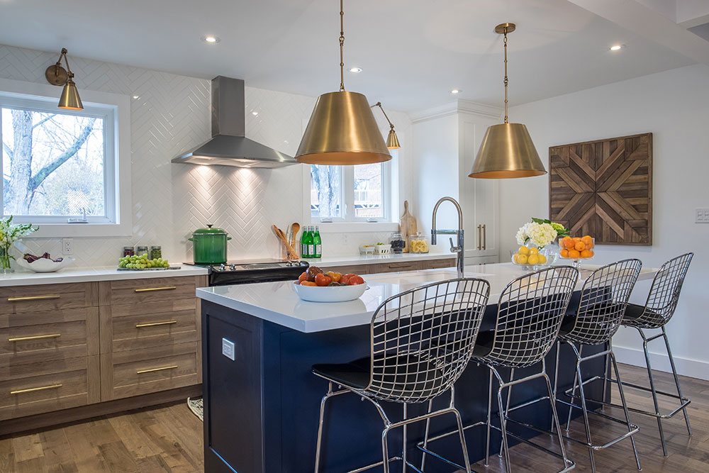 Modern kitchen with dark blue island, brass pendant lights and chrome stools.