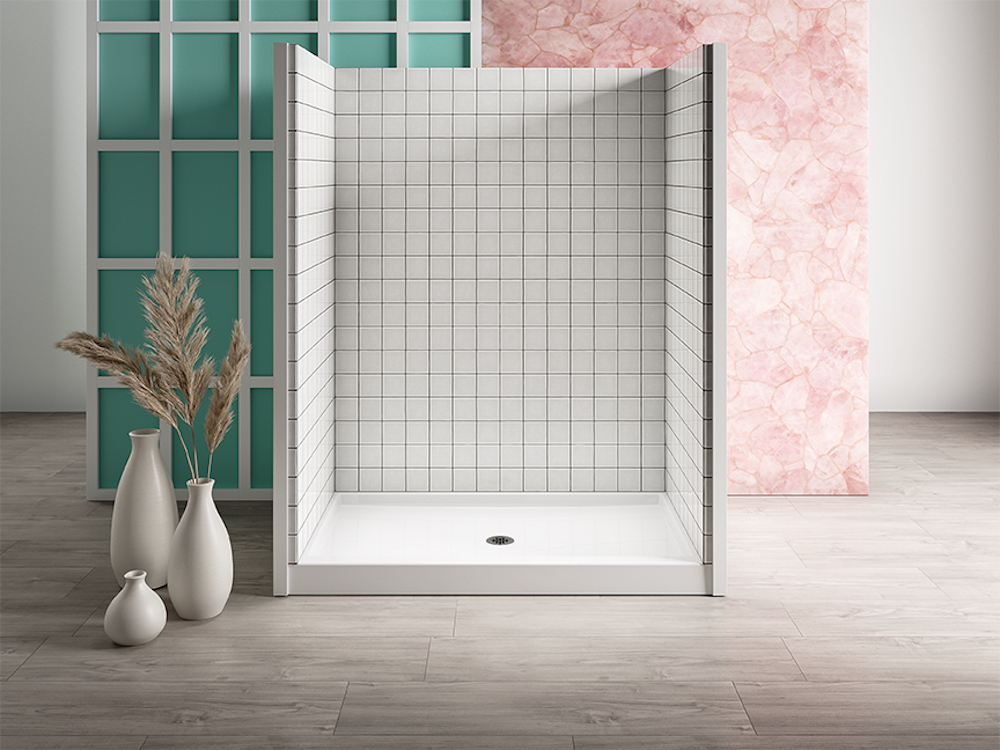 Hytec Kendale™ Shower Base from Splashes Bath & Kitchen with three walls tiled in white square tiles sits in a room with grey tile flooring, three white vases on the floor with pampas grass in one, and a green and white wall and a pink patterned paneled walls sit behind it