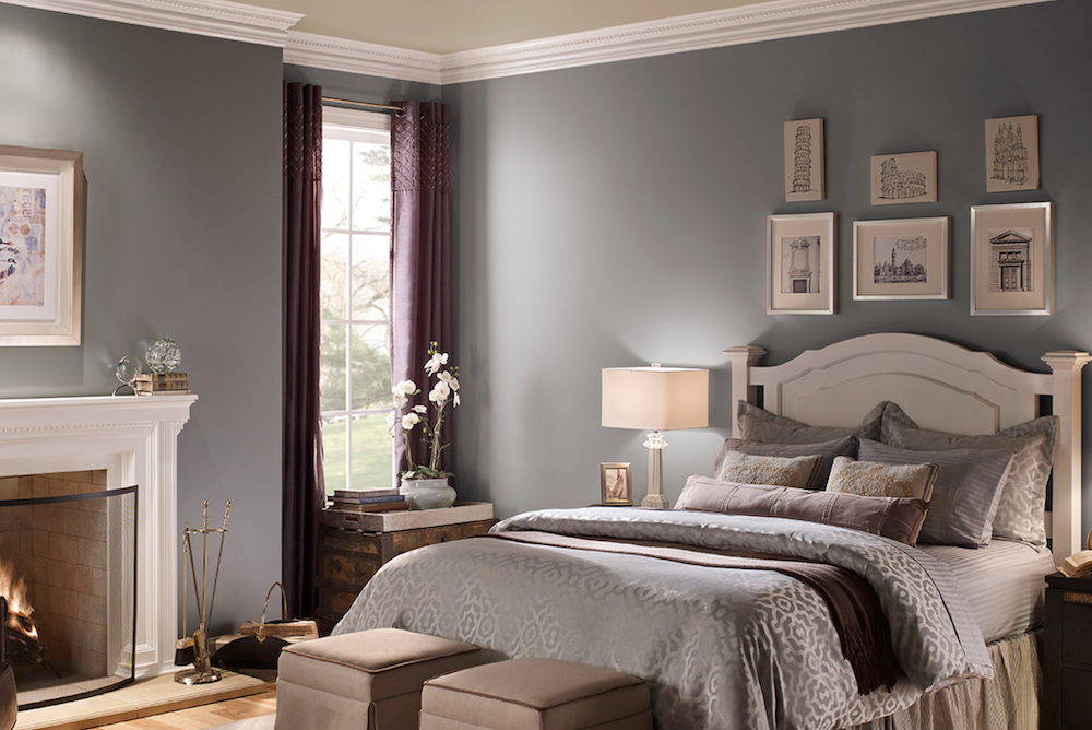 Beautiful bedroom with a white ornate bed, grey green bedclothes, a lit fireplace, purple drapes, and walls painted in BEHR Dark Pewter PPU18-04, Cameo White MQ3-32 and Sandstorm N310-3