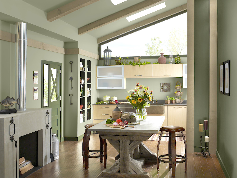 Traditional kitchen with large wooden farmhouse table in the centre and BEHR’s green Ecological S380-6 paint on the walls