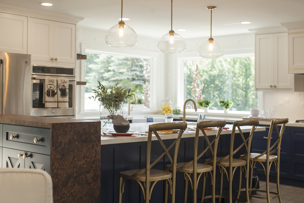 Modern kitchen with three gold pendants lights and a large white kitchen island surrounded by four gold chairs