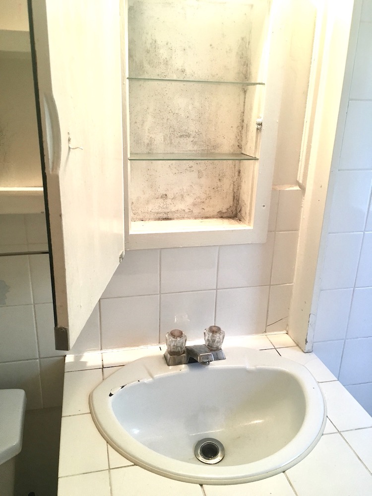 Gross white bathroom sink, vanity and old medicine cabinet with cracks, chips and mold stains