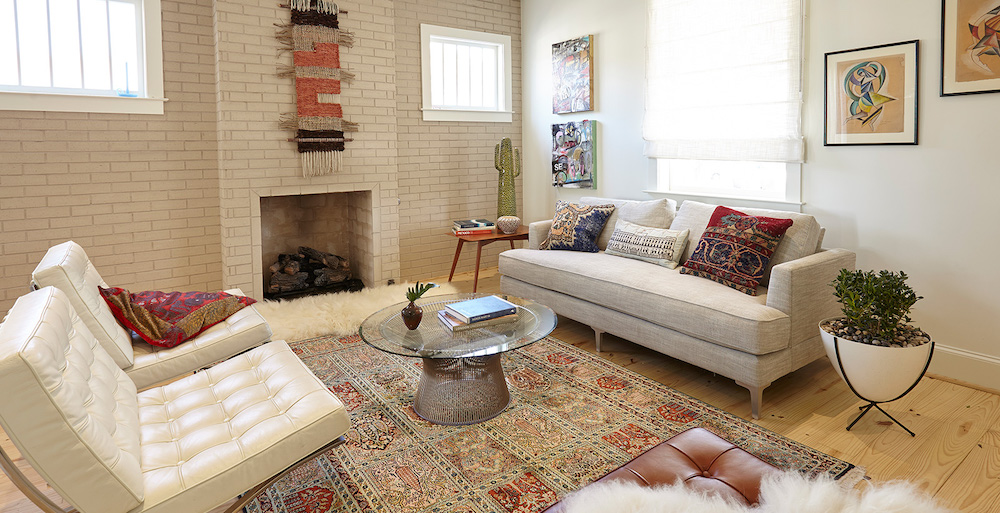 An eclectic living room decorated in the bohemian style with a woven wall hanging above the fireplace, a Persian rug on the floor, woven throw pillows on the taupe upholstered couch, two white leather reclining chairs, and BEHR Silky White PPU7-12 and Roman Plaster PPU7-10 painted on the walls