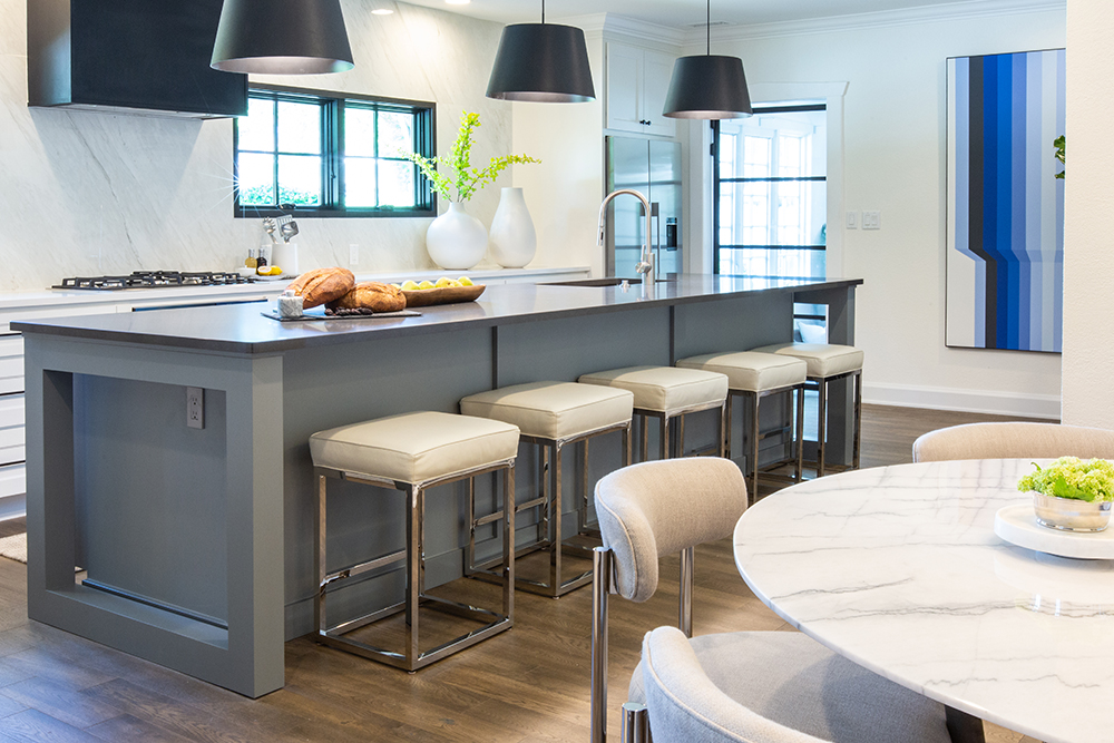 Chic modern kitchen with white cabinets, a high end stovetop, large grey centre island, three black over counter pendant lamps, and a black square oven hood