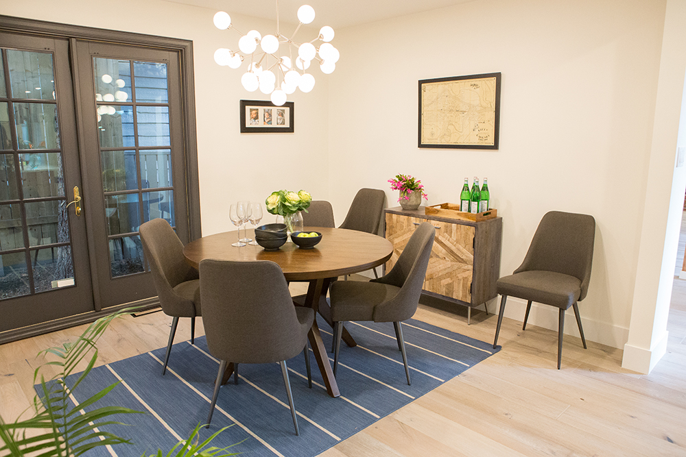 Charming dining room featured on The Property Brothers on HGTV with a round table and four grey upholstered chairs on a blue striped rug over light wood floors, and a multi globe chandelier