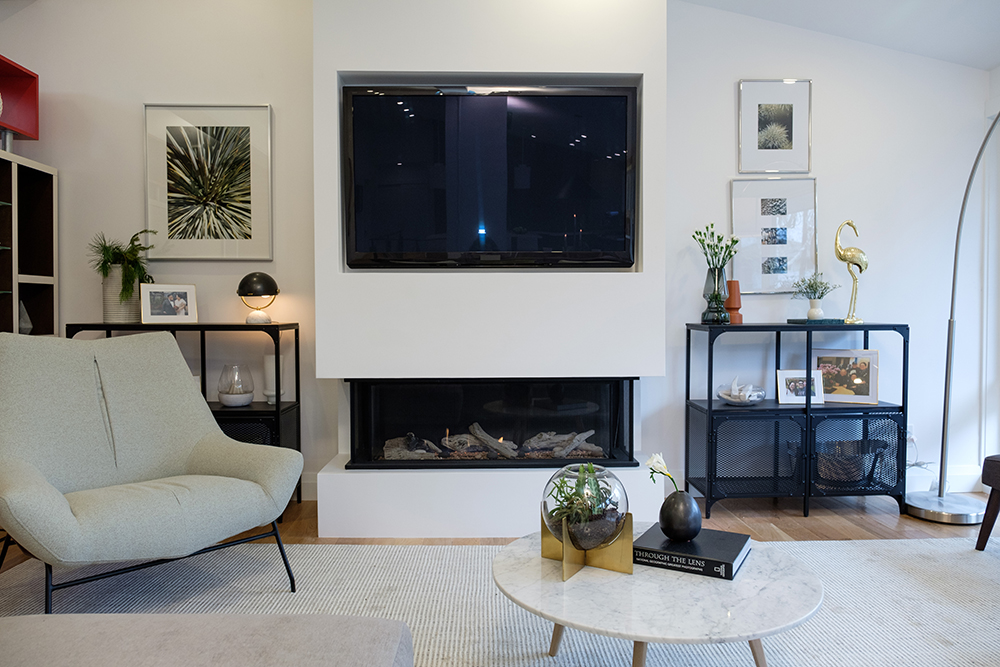Large tv set on a white wall with gas fireplace and large white chair