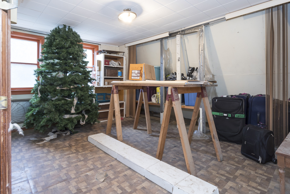 Dirty room with sticker parquet floors, a wooden workhorse and an old faux Christmas tree