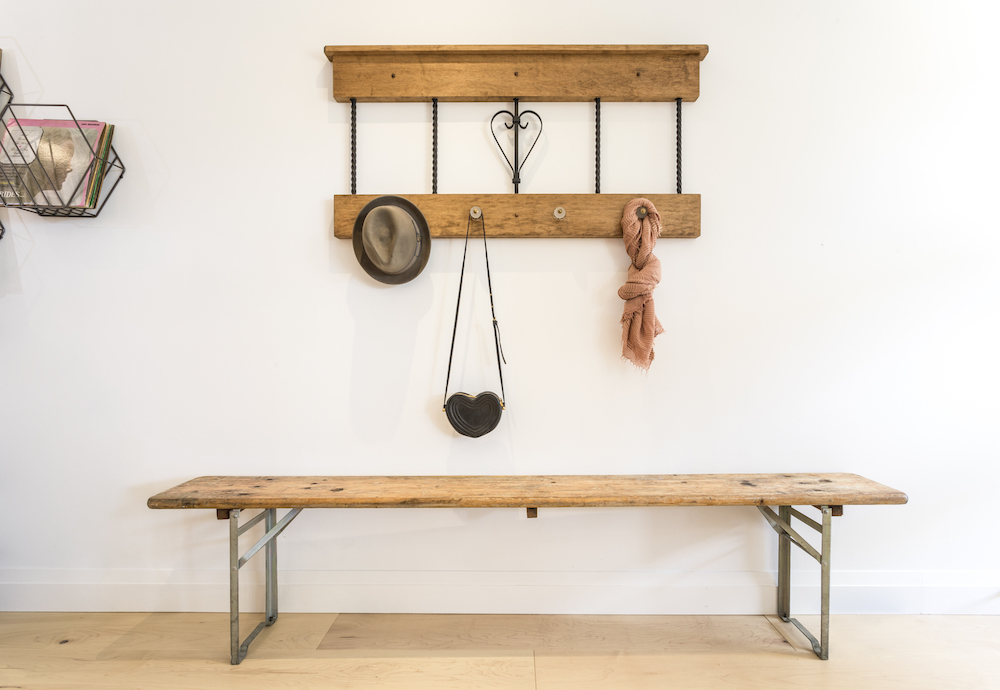 DIY coat rack hangs on the wall with a hat, scarf and purse above a wooden bench