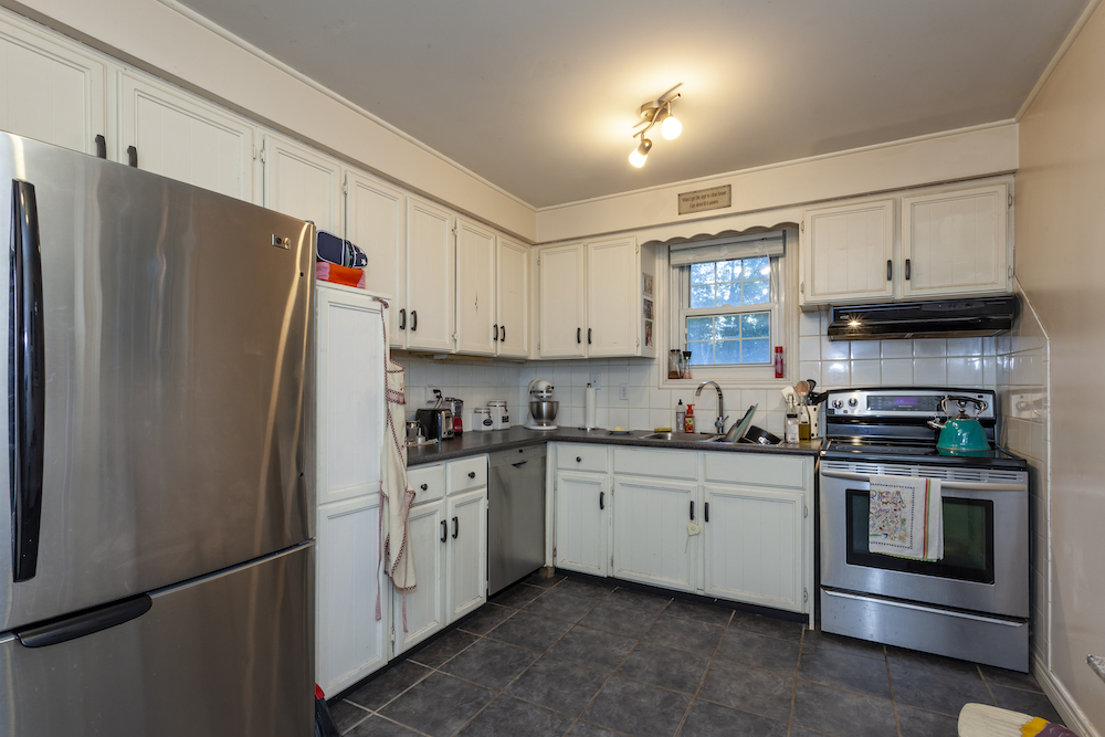 Old boring white kitchen with dark grey tiled floor and stainless steel appliances