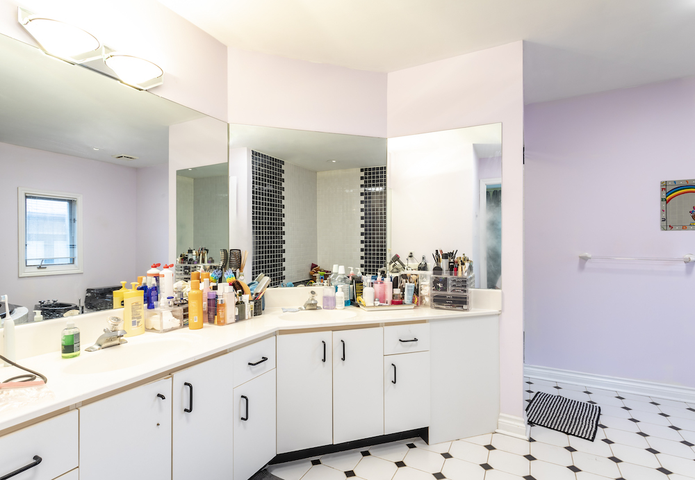 1980s bathroom with black and white tiled floors, white broken cabinets and an overcrowded vanity