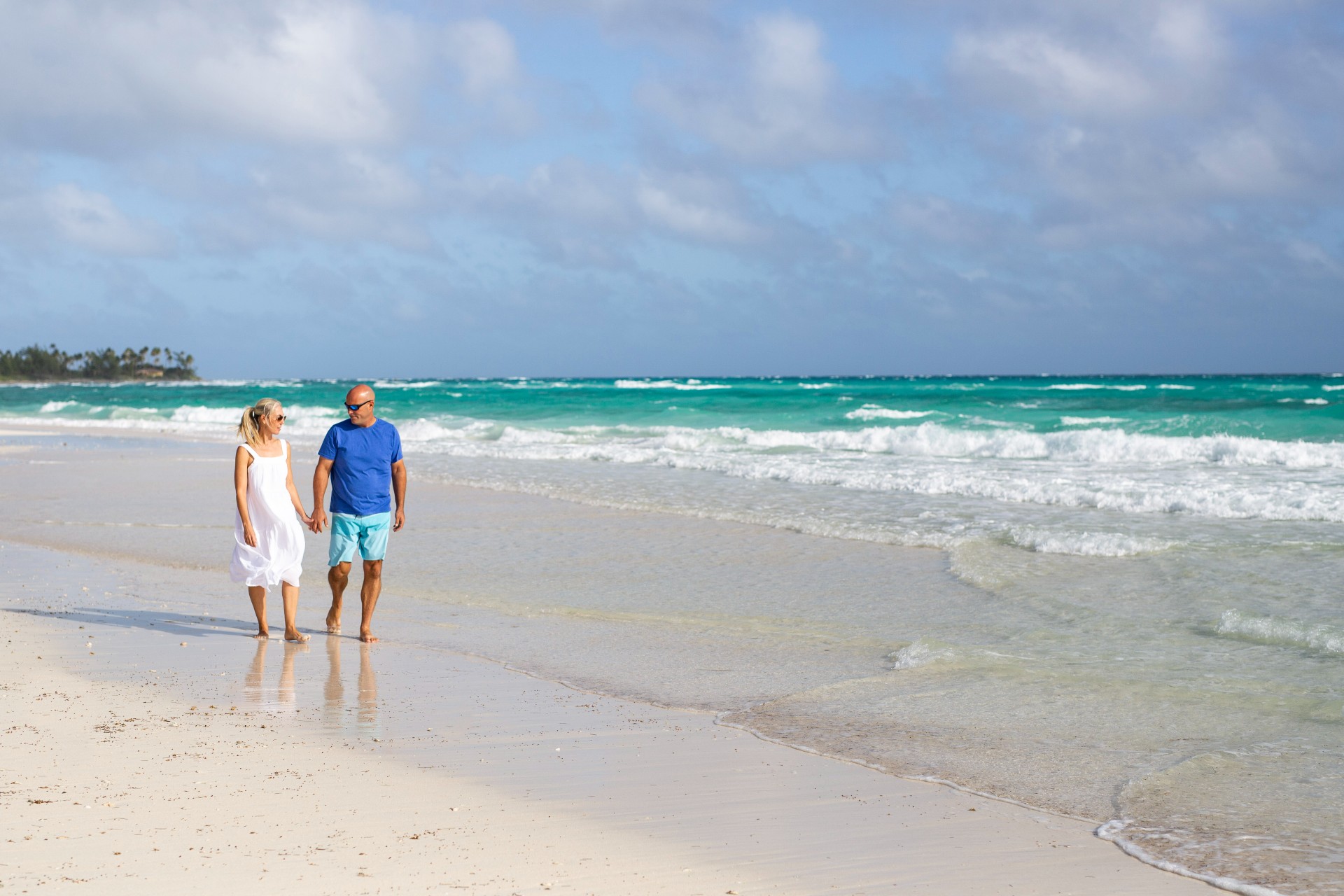 Sarah and Bryan Baeumler walk along beach shore holding hands