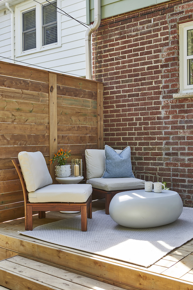 wooden backyard deck with grey chairs and rug in front