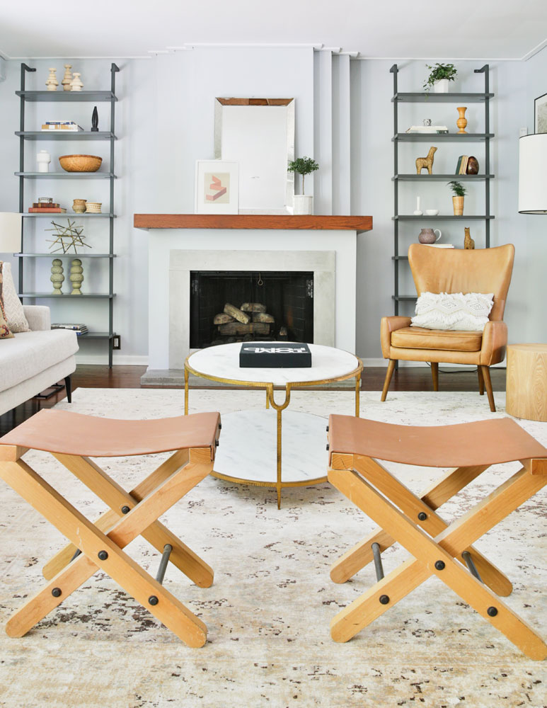 tan leather and wood camp stools in foreground of living room fireplace