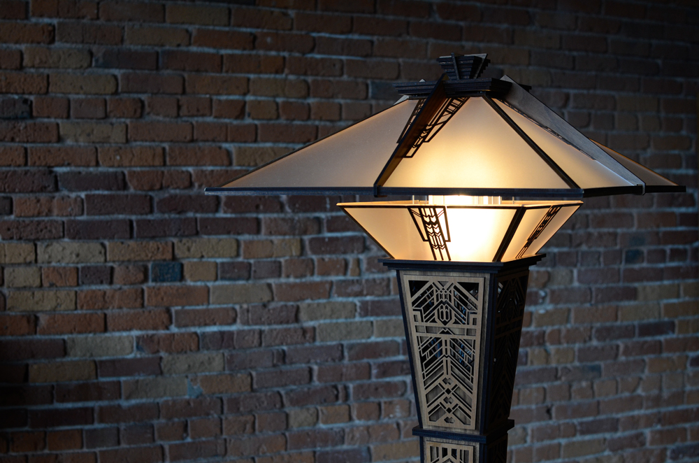 An intricate, carved lamp with wooden base against an exposed brick wall
